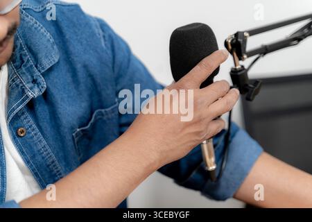 Focused young man speaking into a microphone while recording a podcast in a professional studio environment. Stock Photo