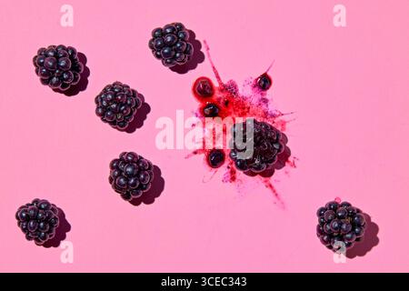 Smashed blackberry with juice and whole blackberries next to it on pink background Stock Photo