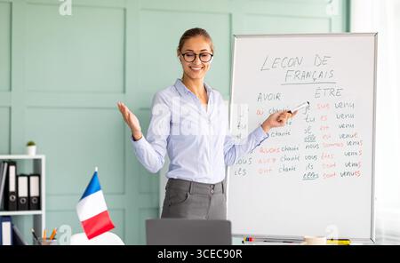 Young positive teacher conducting French lesson on web, talking to laptop webcam, explaining grammar rules to students Stock Photo