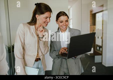 Two professionals collaborate on a laptop in a modern office, showcasing teamwork and creativity Stock Photo