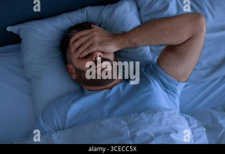 Man Covering Face With Hand Lying Not Sleeping In Bedroom Stock Photo