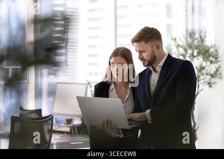 Couple of serious young business colleagues using laptop computer Stock Photo