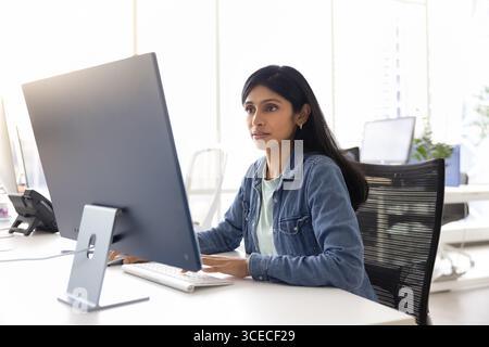 Focused young Indian specialist woman working at computer monitor Stock Photo