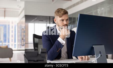 Pensive serious young executive man working at desktop in office Stock Photo