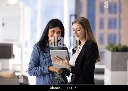Two happy multiethnic female coworkers using digital technology Stock Photo