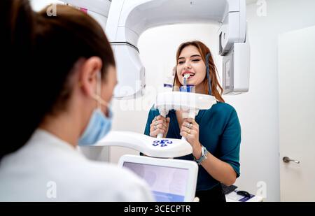 A dentist performs a panoramic dental X-ray on a patient at a modern clinic. The patient is positioned in the X-ray machine while the dentist observes Stock Photo