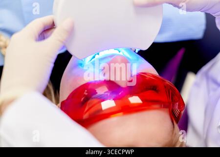 A patient undergoes a UV dental treatment at a clinic, wearing protective eyewear. The procedure involves advanced light technology to enhance oral ca Stock Photo