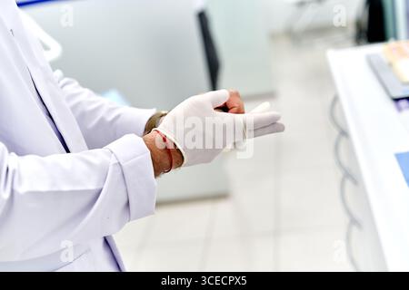 Dentist carefully putting on sterile gloves in a modern dental clinic. White lab coat and professional setting ensure a clean and hygienic environment Stock Photo