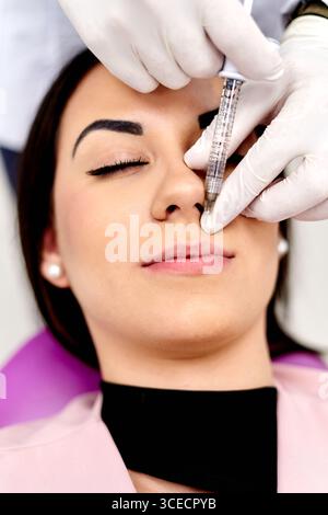 A close-up image of a cosmetic facial procedure, showing a professional administering an injection with precision. The patient appears calm and relaxe Stock Photo