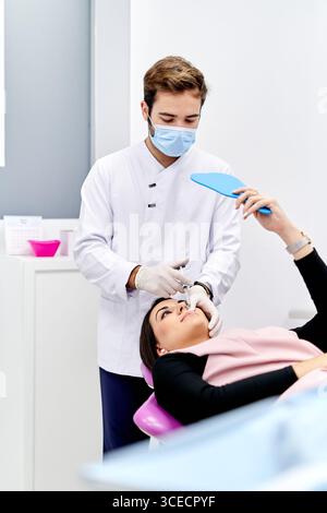 A doctor in a medical office administers a hyaluronic acid injection to a patient. The doctor wears a mask and sterile white gloves, ensuring a clean Stock Photo