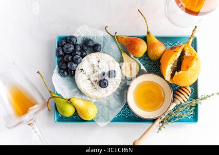 A beautifully arranged gourmet platter featuring creamy brie cheese, fresh blueberries, sliced pears, and a drizzle of honey on a decorative tray, acc Stock Photo