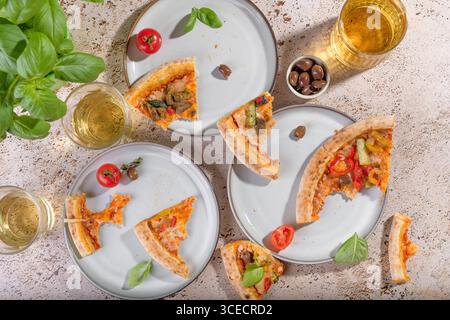 Top view of rustic vegetarian pizza slices with zucchini, eggplant, bell peppers, and basil. Accompanied by olives and refreshing drinks on a rustic t Stock Photo