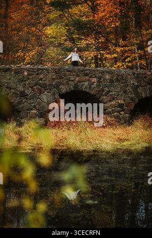 A woman stands serenely on a stone bridge in Quebec, Canada, surrounded by the vibrant colors of autumn. The scene reflects the peacefulness of a quie Stock Photo