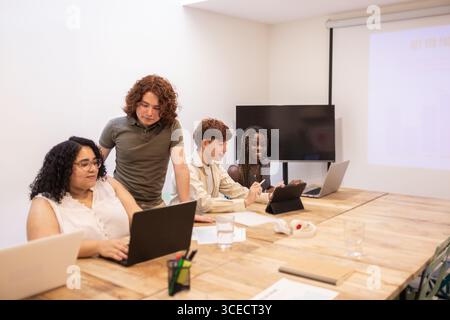 A diverse group of young professionals collaborating in a modern coworking space. They are using laptops and tablets, showcasing an inclusive and tech Stock Photo