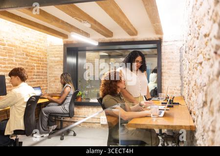 A diverse group of coworkers engaging in a collaborative workspace with laptops. The image highlights the inclusivity and multicultural environment of Stock Photo