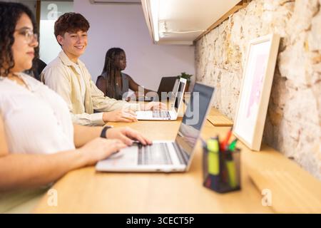 A group of professionals engaging in collaborative work at a shared office space. They are focused on tasks, using laptops, fostering teamwork in a co Stock Photo