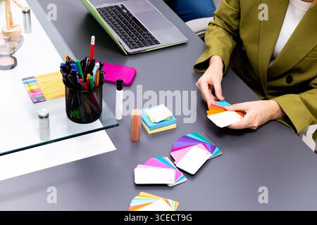A professional image consultant arranges an array of colorful swatches on a table. Tools like stationery and a laptop are visible, highlighting a work Stock Photo
