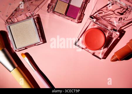 Top view of vibrant pink makeup set, including eyeshadow palette, blush, lipstick, and brushes, arranged on a pastel pink surface. Acrylic cases refle Stock Photo