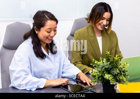 Two professional women engaging collaboratively in a modern consulting workspace, using a tablet and laptop for effective communication and teamwork i Stock Photo