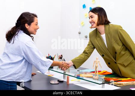 A vibrant image of two women shaking hands in an image consulting setting. They smile warmly, embodying professionalism and collaboration, with colorf Stock Photo