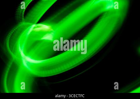 A dynamic abstract image featuring swirling green light trails on a dark background. The neon-like glow creates a sense of movement and energy, perfec Stock Photo