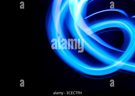 A captivating abstract image of swirling blue neon light streaks set against a dark background. The flowing lines create an energetic and dynamic visu Stock Photo
