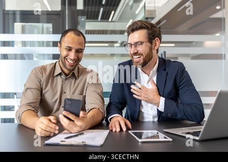 A lively meeting of two colleagues in a modern office, sharing a conversation while using a smartphone for collaboration. Stock Photo