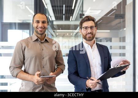 Two individuals dressed in professional attire meet in a contemporary office for a business discussion. They appear positive and focused on their task. Stock Photo