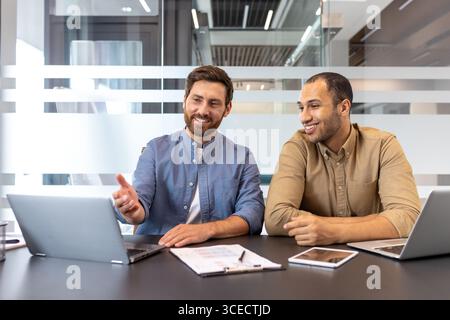 Two professionals engaged in discussion, working together with laptops and documents in a modern office. Stock Photo
