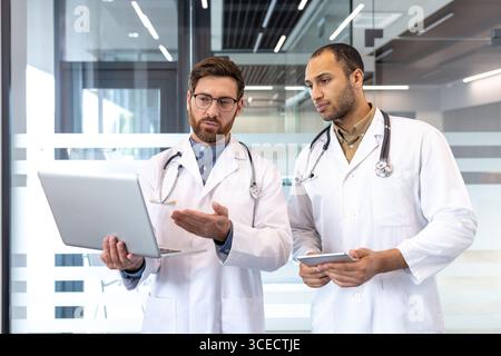 Two professional doctors are collaborating and reviewing patient information using a laptop, in a contemporary and professional medical facility environment Stock Photo