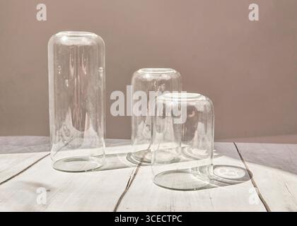 Three transparent glass jars are placed upside down on a textured wooden surface, casting soft shadows. The minimalist setting emphasizes simplicity a Stock Photo