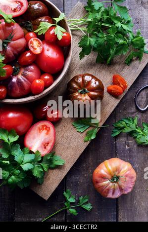 Top view of fresh tomatoes and parsley on a rustic wooden table. A wooden bowl overflows with red tomatoes, while vibrant green parsley adds a fresh t Stock Photo