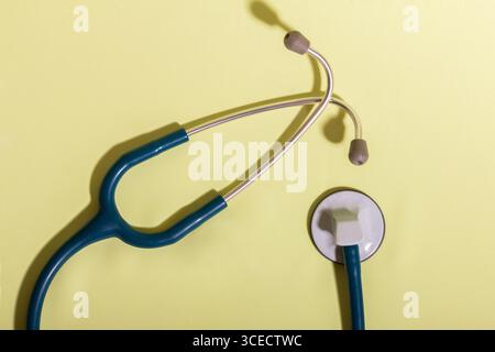 A medical stethoscope with a blue tube and gray earpieces is placed on a light yellow background, symbolizing healthcare, diagnostics, and sanitary ma Stock Photo