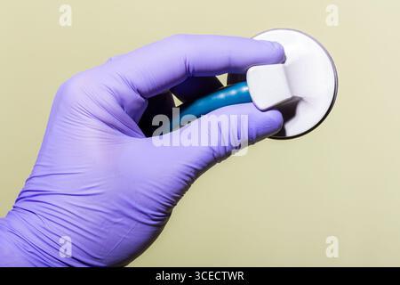 A gloved hand gently holding a stethoscope on a neutral background. The image represents healthcare and sanitary practices, focusing on safety and hyg Stock Photo