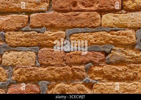 Close-up view of a rustic brick wall, showcasing its unique textured pattern with rough surfaces. The orange and brown hues enhance its natural appear Stock Photo
