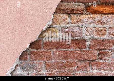 Close-up of an aged brick wall with a section of pink plaster peeling away, revealing the rough texture beneath. The exposed bricks add an element of Stock Photo