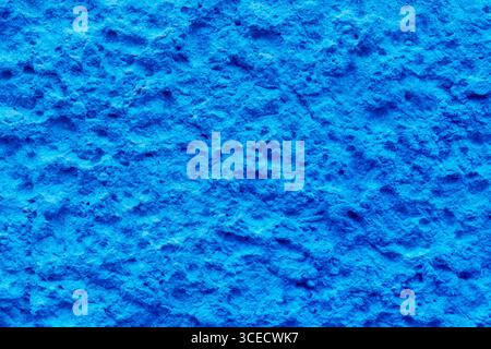 Close-up view of a bright blue textured wall showing a rough, uneven surface with intricate patterns. The vivid color and details create an abstract, Stock Photo