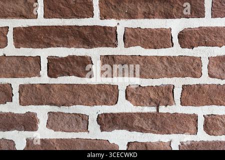 Close-up view of a red brick wall showcasing a rugged, textured surface with bright white mortar joints. The bricks' roughness and color offer a strik Stock Photo