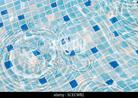 A close-up image of mosaic tiles under clear, rippling water, creating a serene and refreshing summer vibe. The blue and white tiles enhance the calmi Stock Photo