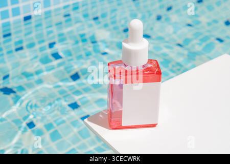 A vivid red serum bottle with a white dropper cap on a white surface beside a blue tiled pool, capturing a bright and refreshing summer vibe. Perfect Stock Photo