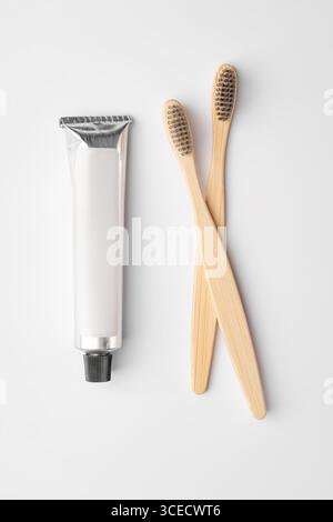 Top view of two bamboo toothbrushes with brown bristles and a metallic toothpaste tube are placed on a clean white surface, highlighting eco-friendly Stock Photo