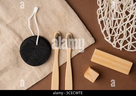 Top view of bamboo toothbrushes, black pumice stone, and wooden soap dish on burlap and brown paper background, featuring eco-friendly toiletries and Stock Photo