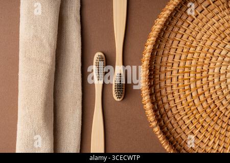 Top view of bamboo toothbrushes on a brown background, accompanied by a woven basket and a linen cloth, highlighting eco-friendly and sustainable bath Stock Photo