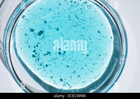 A close-up view of a vibrant blue cosmetic gel with visible bubbles, contained in a circular glass Petri dish on a white background, showing texture a Stock Photo