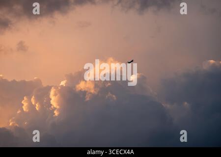 An airplane silhouette gracefully soars through a breathtaking sky filled with vibrant orange and gray clouds, capturing the serene and dramatic essen Stock Photo