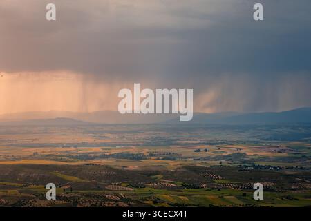 A dramatic storm approaches the Alcarria region in Spain, casting a shadow over verdant fields and rolling hills during a picturesque spring sunset. A Stock Photo