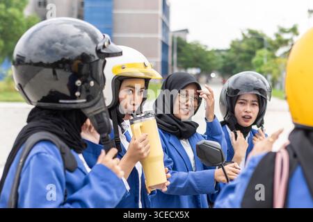 A group of Asian Muslim students wearing helmets and school uniforms gather on campus, preparing for class. They appear engaged and ready for a day of Stock Photo