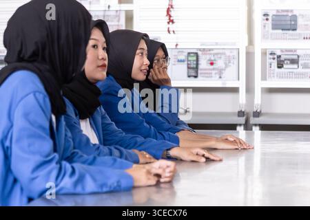 Asian Muslim students in blue uniforms attentively participate in a classroom setting, symbolizing education and diversity. They sit side by side, rea Stock Photo