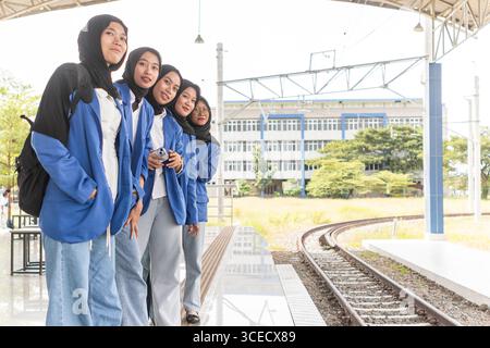 A group of Asian Muslim students dressed in blue blazers and black hijabs are standing together, smiling and looking confident outside their education Stock Photo