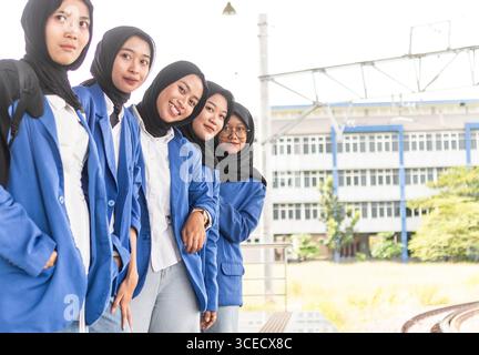 A group of Asian Muslim students dressed in blue blazers and black hijabs are standing together, smiling and looking confident outside their education Stock Photo